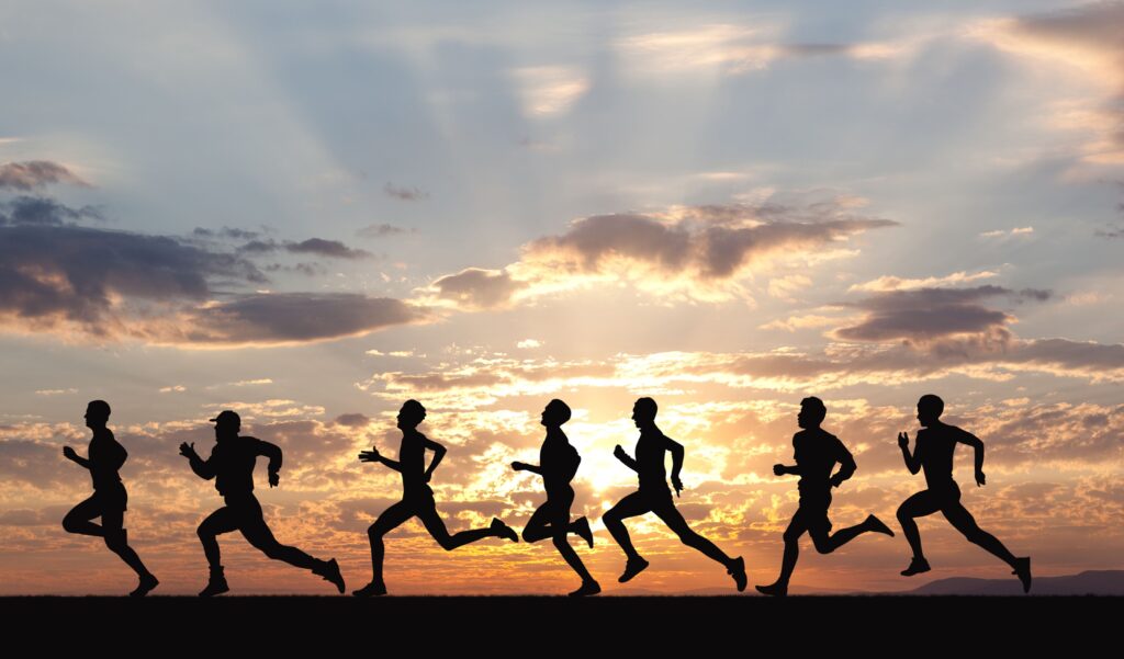 Silhouettes of seven runners in mid-stride against a sunset sky, conveying motion and teamwork in an outdoor setting.